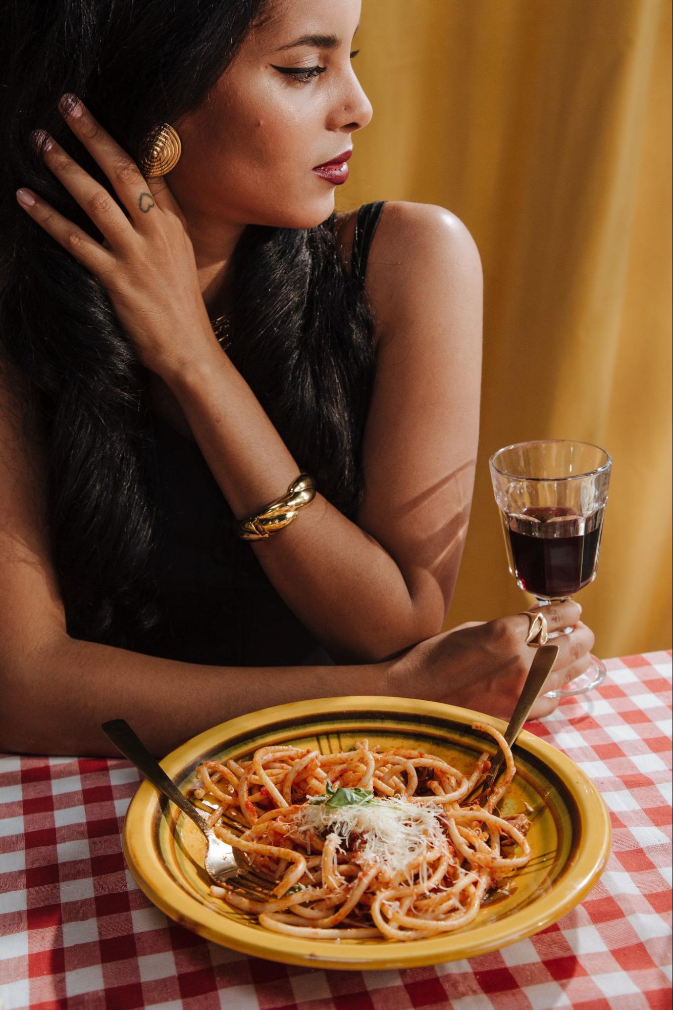 Woman behind her plate of pasta holding a glass of red wine