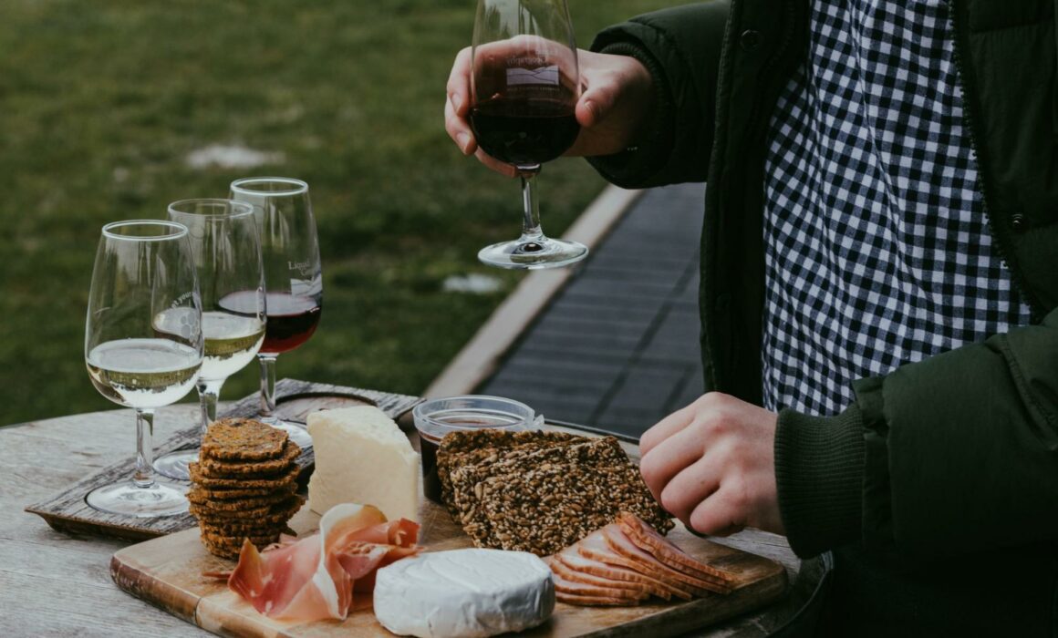 Man holding a glass of wine and selecting items from a cheese board