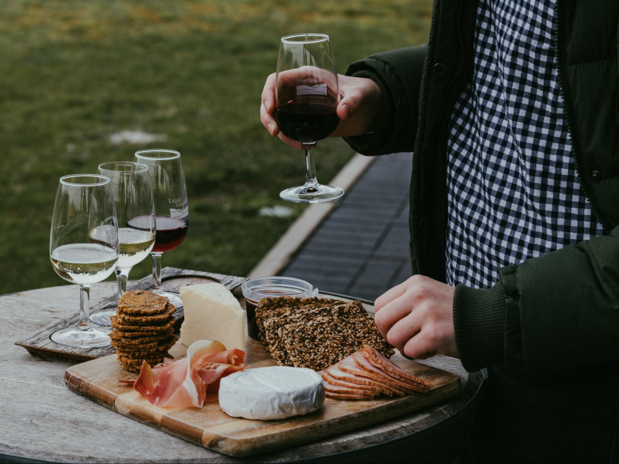 Man holding a glass of wine and selecting items from a cheese board